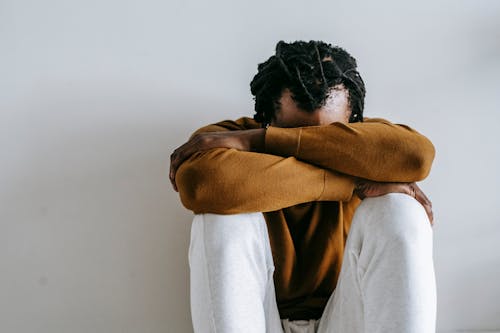 Free Unrecognizable hopeless African American male in casual outfit with dreadlocks sitting leaned on hands in daylight Stock Photo