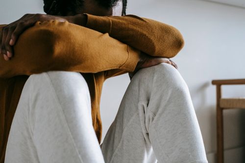 Free Crop anonymous abandoned African American male in casual outfit sitting leaned on hands at home Stock Photo