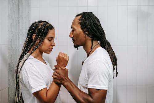 Free Side view of young muscular African American male holding arm of female partner while struggling in house Stock Photo