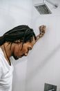 Side view of young sorrowful African American male with dreadlocks looking down under water flow in bathroom