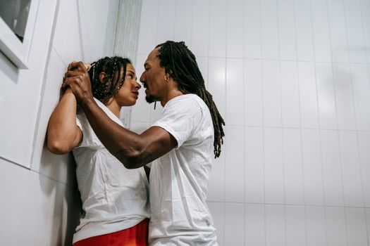 Low angle side view of young violent ethnic male with dreadlocks disputing with girlfriend while looking at each other at home
