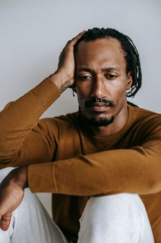 一名穿着棕色毛衣的男子若有所思地坐着，将头枕在手上，神情若有所思