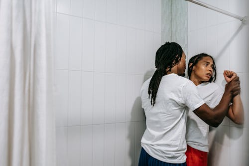 Free Angry African American man with dreadlocks grabbing hands of scared woman and pressing against tiled wall during argument in bathroom Stock Photo