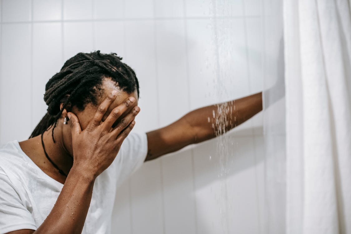 Sad African American man covering face with hand in shower cabin