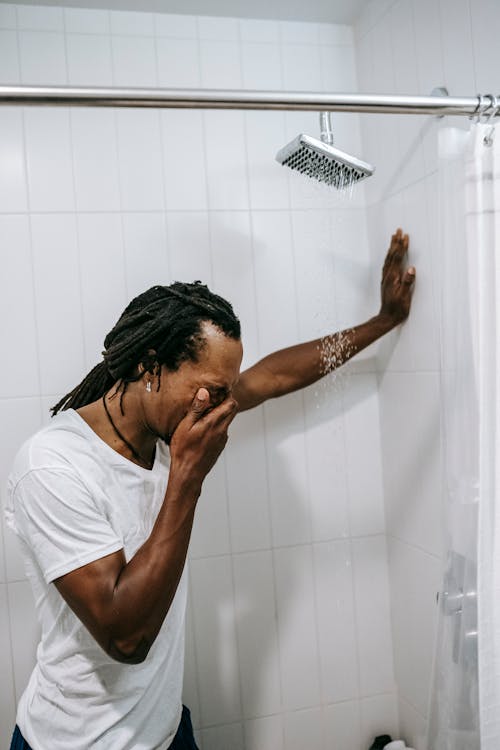 Отчаянный молодой черный мужчина закрывает лицо рукой и плачет в ванной
