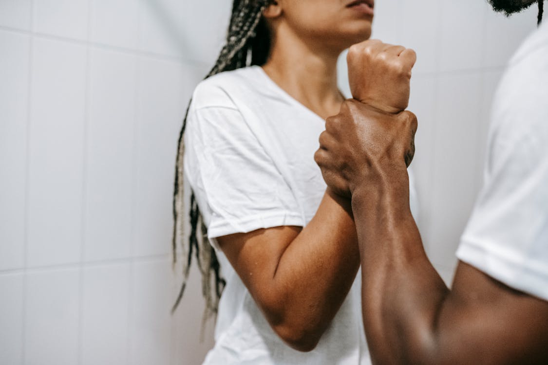 Side view of crop unrecognizable aggressive African American male holding wrist of scared wife while quarreling together in bathroom