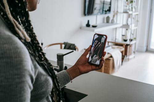 Free Crop unrecognizable African American lady with long braids having video call on mobile phone with upset boyfriend covering face with hands while standing in modern kitchen Stock Photo