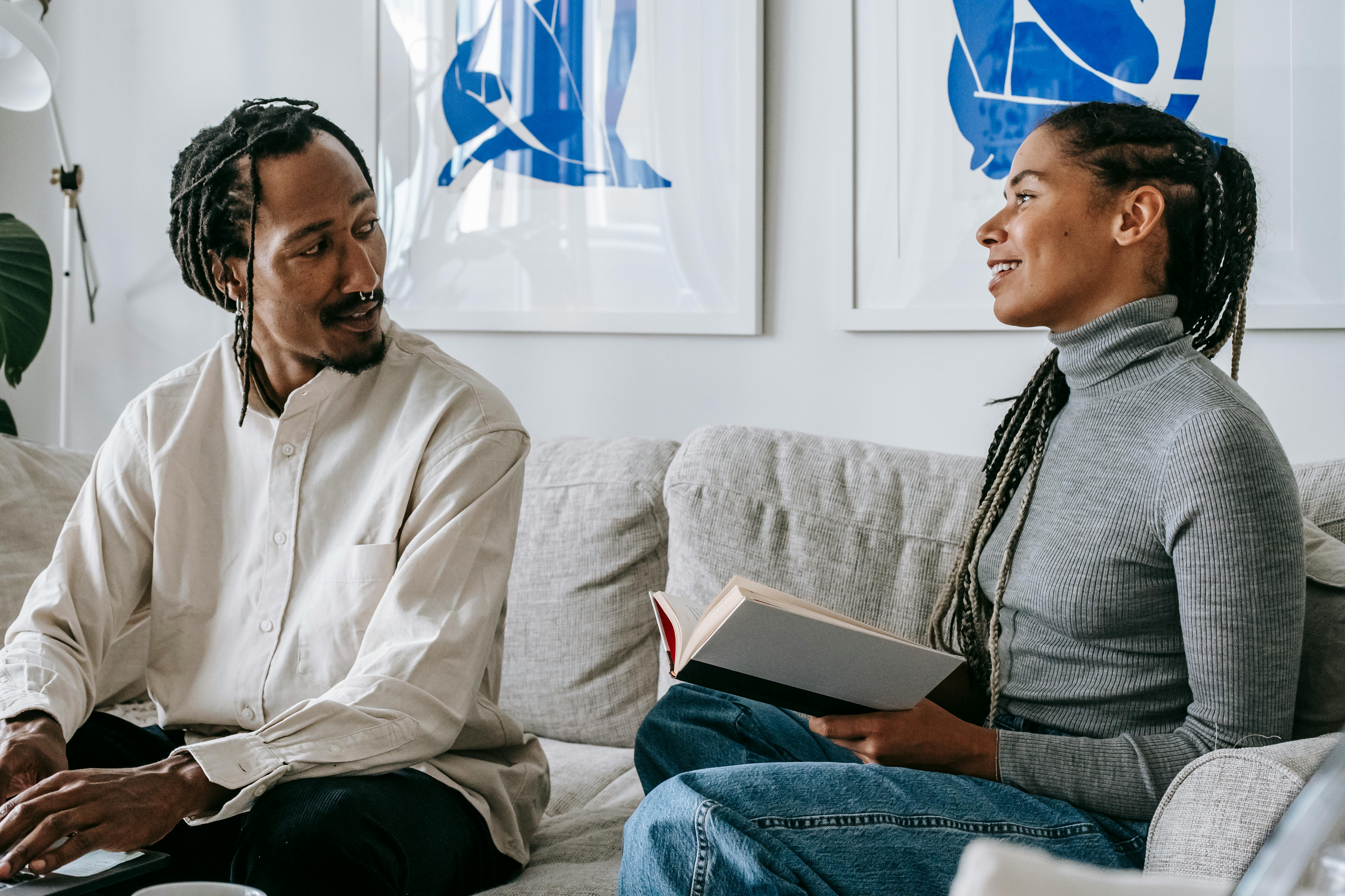 happy young ethnic couple chatting while sitting on couch at home