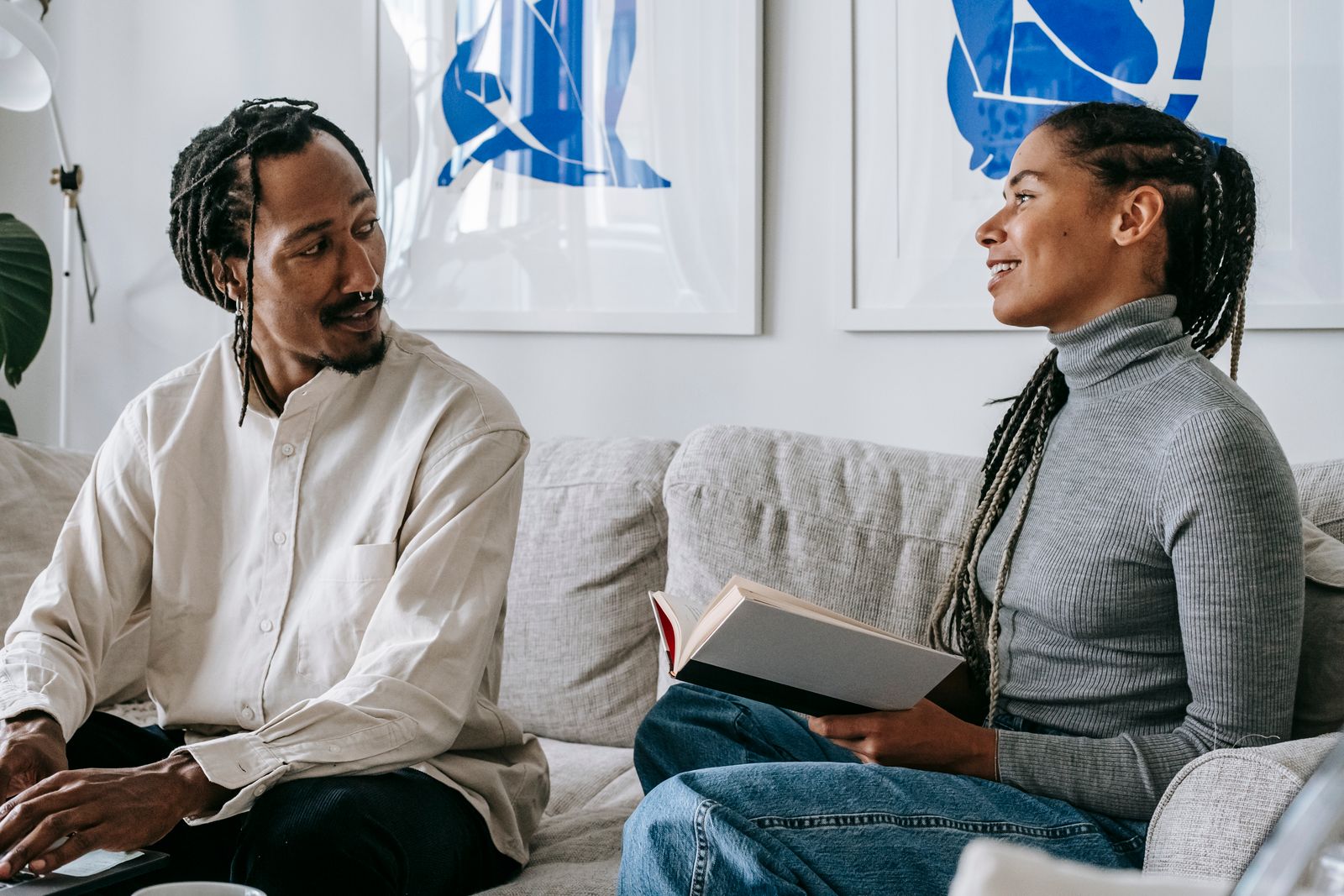 Two people talking on a sofa, one holding an open book