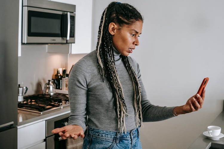 Confused Young Ethnic Female Having Video Conversation On Mobile Phone At Home