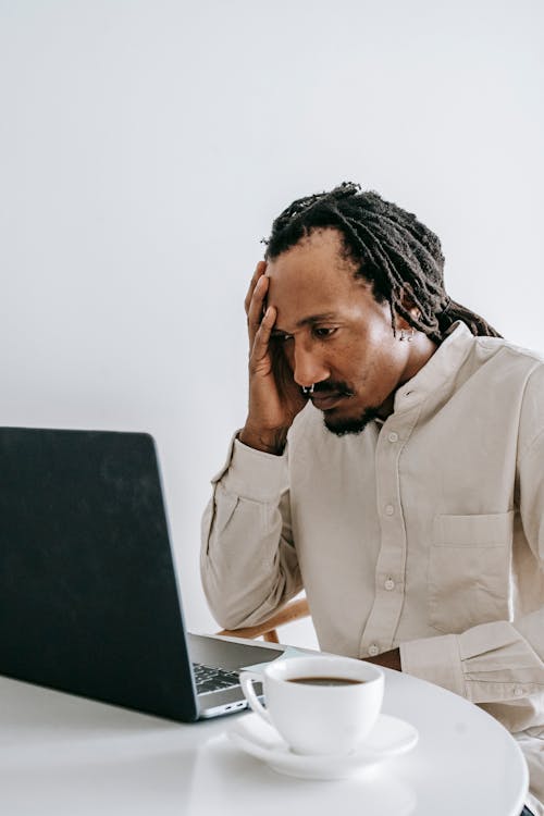 Worried young black man working online on laptop in kitchen