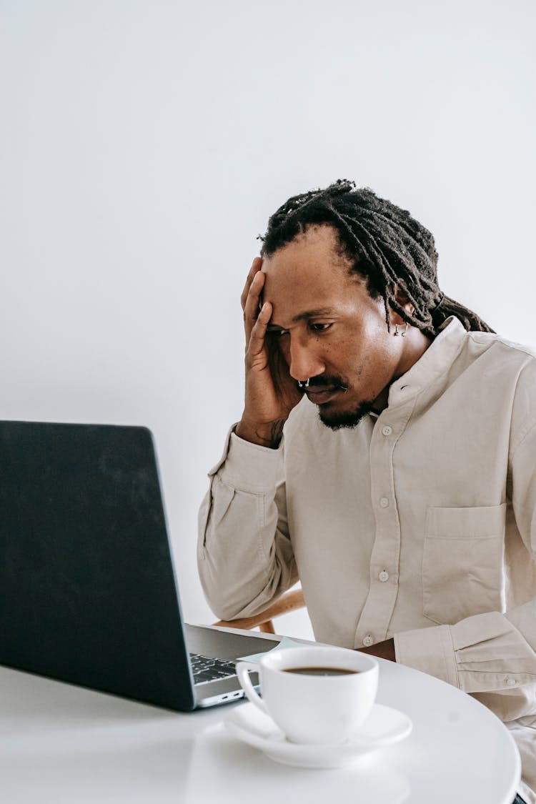 Worried Young Black Man Working Online On Laptop In Kitchen