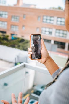 From above of crop unrecognizable ethnic female standing on balcony and having video chat with boyfriend via mobile phone