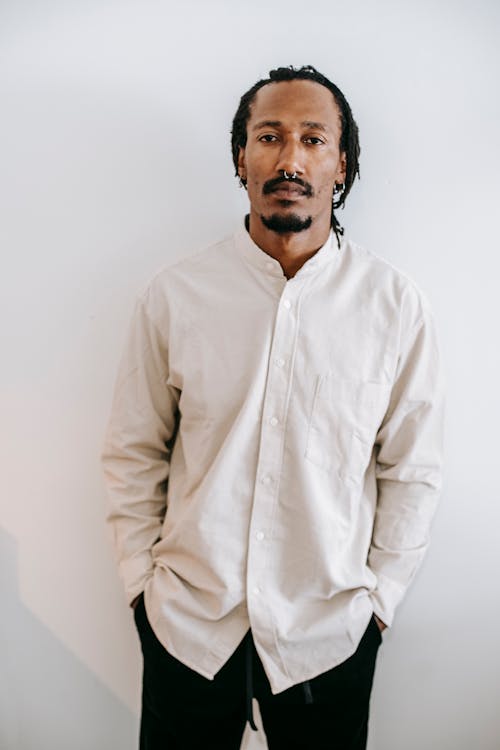 Free Serious African American male in casual outfit holding hands in pockets while standing against white background and looking at camera Stock Photo