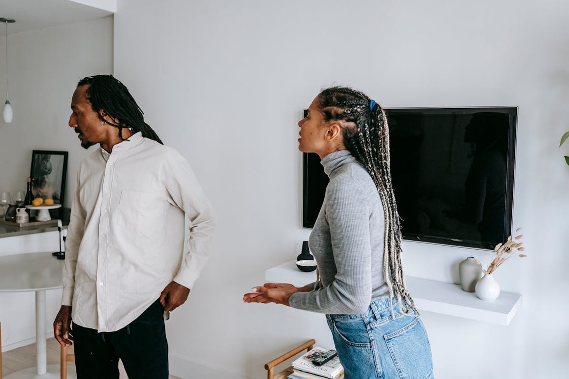 Emotional black couple standing in cozy apartment and having conflict while spending time together