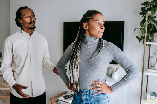 Unhappy African American couple quarreling while spending time together in light modern apartment
