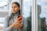 Low angle of concerned ethnic female with smartphone in stressful situation near glass wall