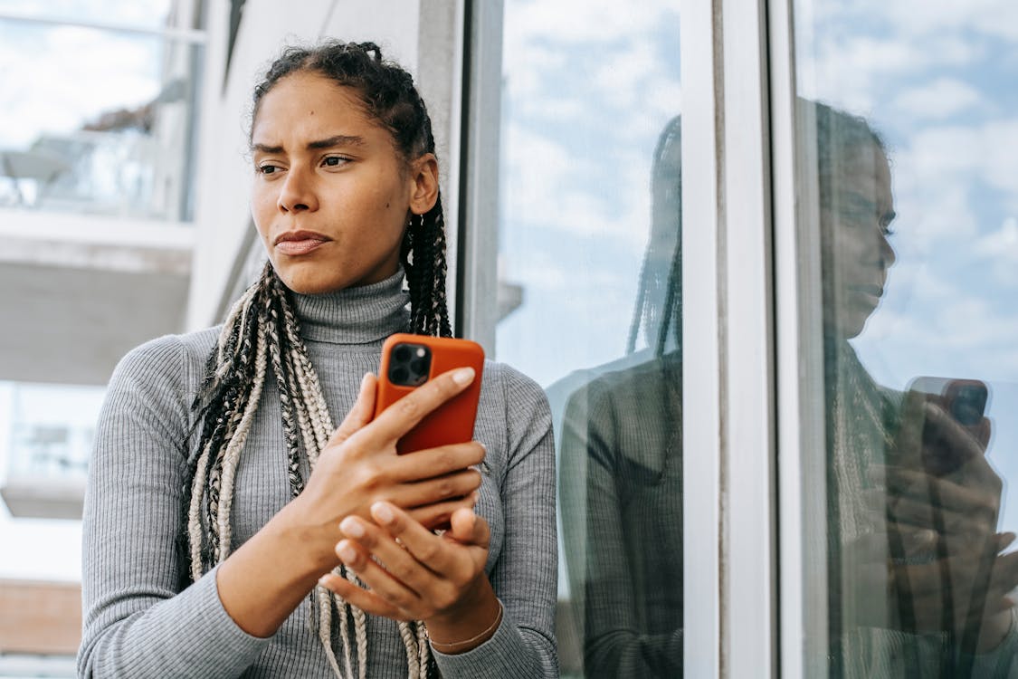 外で携帯電話を持ち、顔をしかめながら横を見る女性。