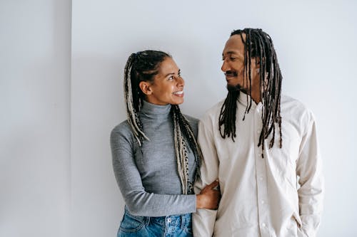 Free Cheerful ethnic couple smiling to each other while holding hands and looking at each other with love Stock Photo