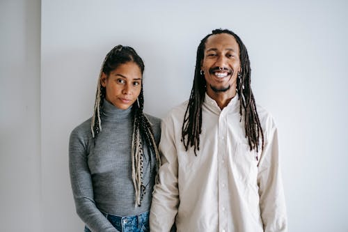 Delighted ethnic man with braids smiling widely while standing near girlfriend in casual clothes