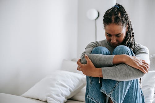 Upset ethnic woman embracing knees on bed