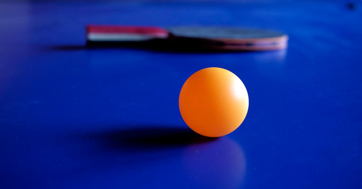 Vibrant orange ping pong ball with a table tennis racket on a blue table, emphasizing sport and leisure.