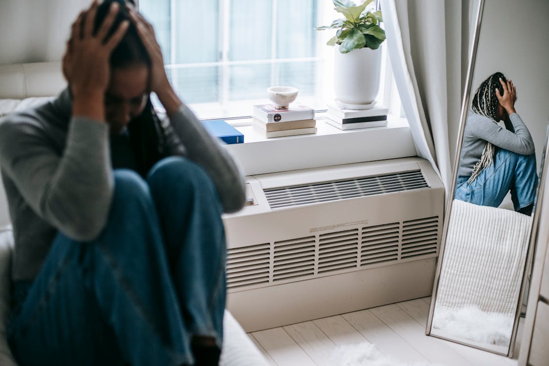 Free Frustrated young female having mental problem reflecting in mirror while sitting alone in room Stock Photo