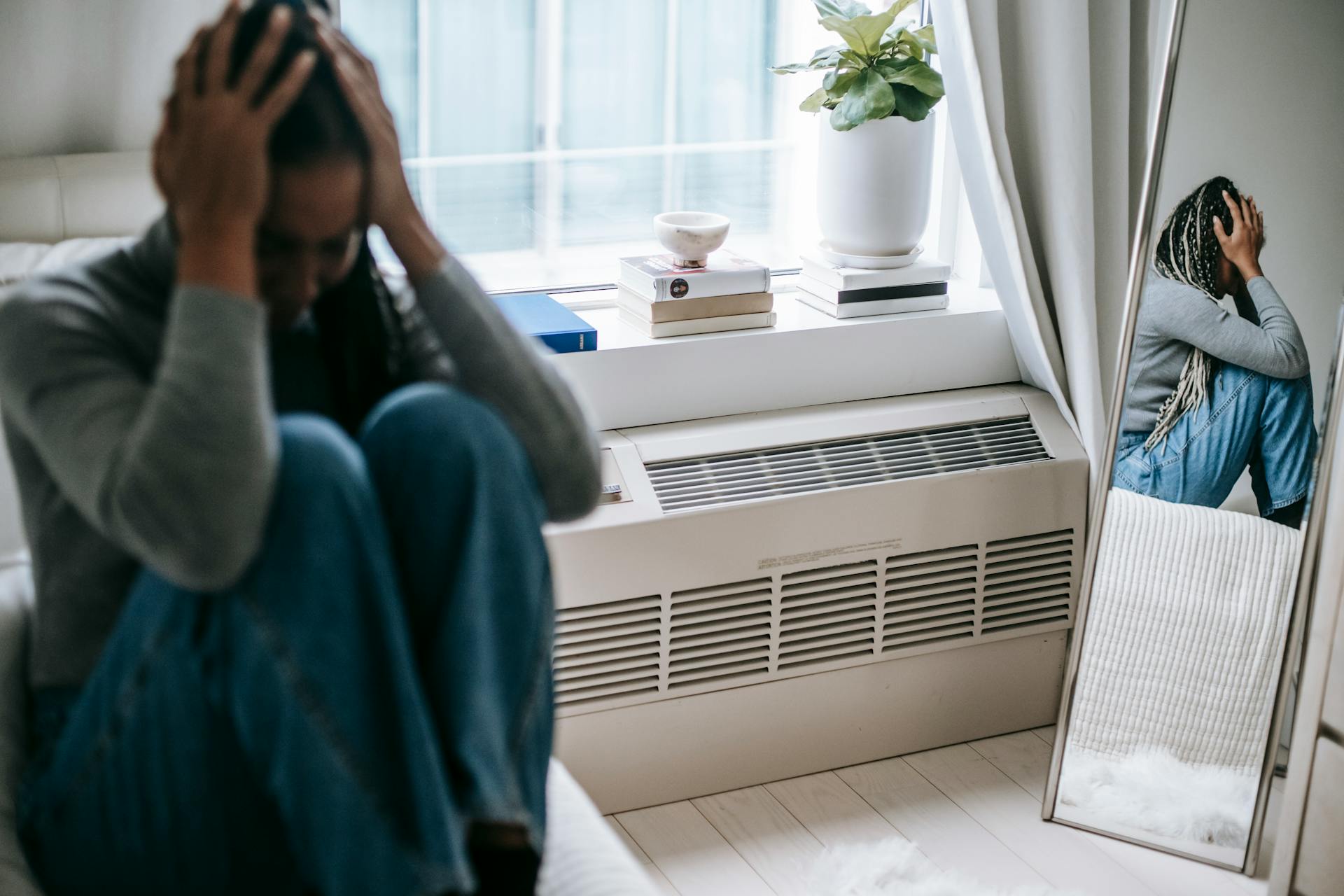 Frustrated young female having mental problem reflecting in mirror while sitting alone in room