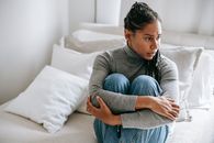 一个女人坐在床上，若有所思地搂着自己的手臂，陷入了深深的沉思