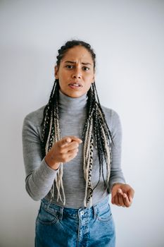 Ethnic female with long braids blaming  pointing with forefinger at camera standing against gray background