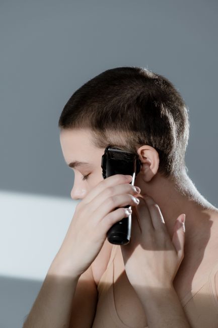 Close-up of a woman trimming her hair with an electric shaver, showcasing short hairstyle.
