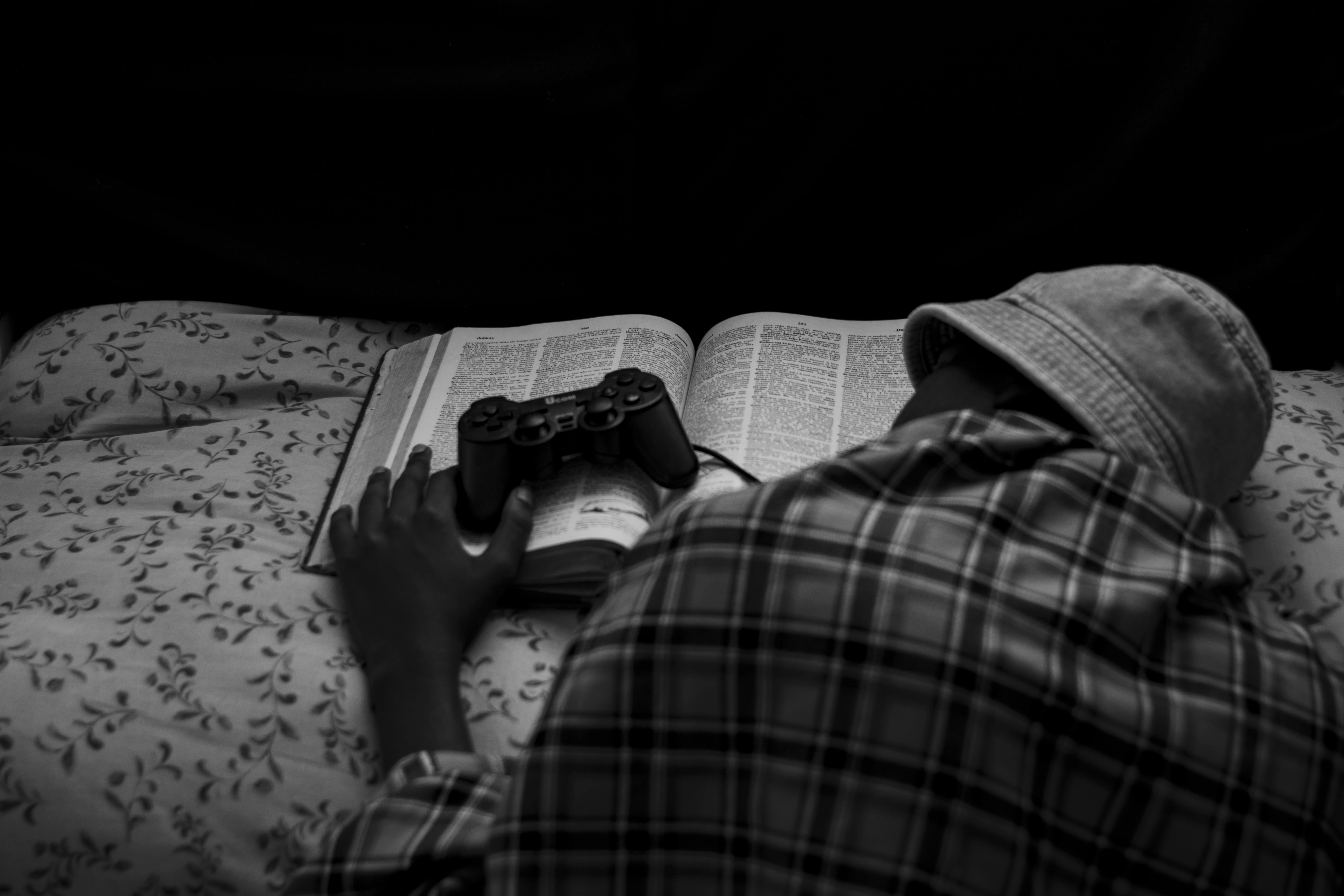 monochrome shot of a person sleeping on a book while touching game console