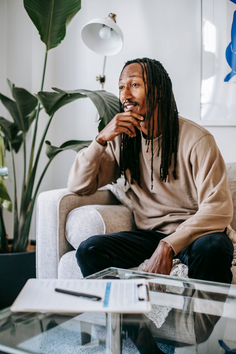 Interested Black Man Touching Chin On Sofa At Home