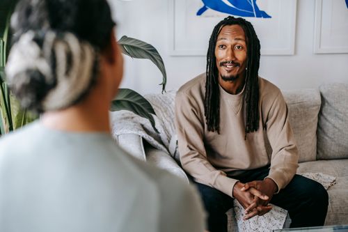 Free Bearded African American male with dreadlocks and clasped hands speaking with crop anonymous female beloved at home Stock Photo