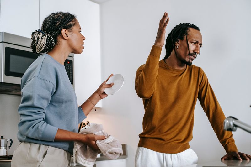 Young dissatisfied African American man with raised arm having conflict with girlfriend in house