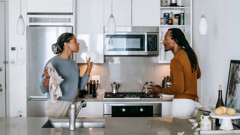 Young black woman talking to annoyed male partner while looking at each other during quarrel in house