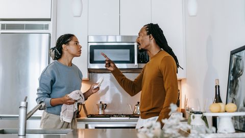 Discontented African American male menacing to female partner with finger up while looking at each other during dispute at home