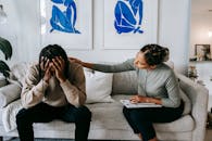 Black woman consoling anonymous unhappy boyfriend on sofa at home