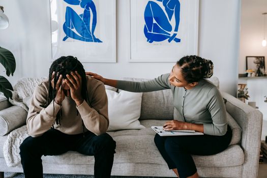Black woman consoling anonymous unhappy boyfriend on sofa at home