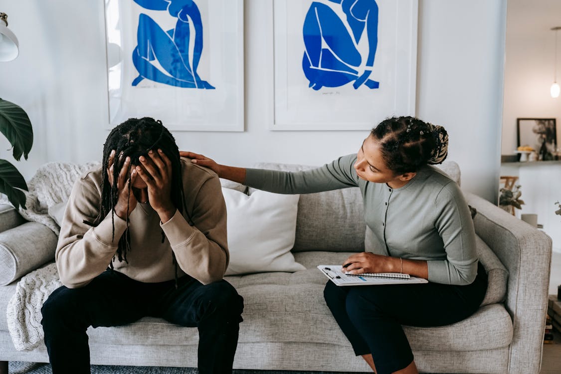 Free Black woman consoling anonymous unhappy boyfriend on sofa at home Stock Photo