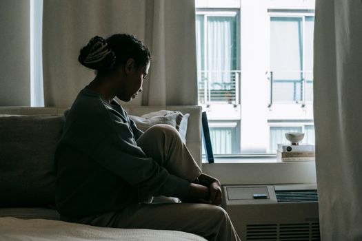 一位年轻女子若有所思地坐在城市公寓的窗前，透着一股孤独的情绪