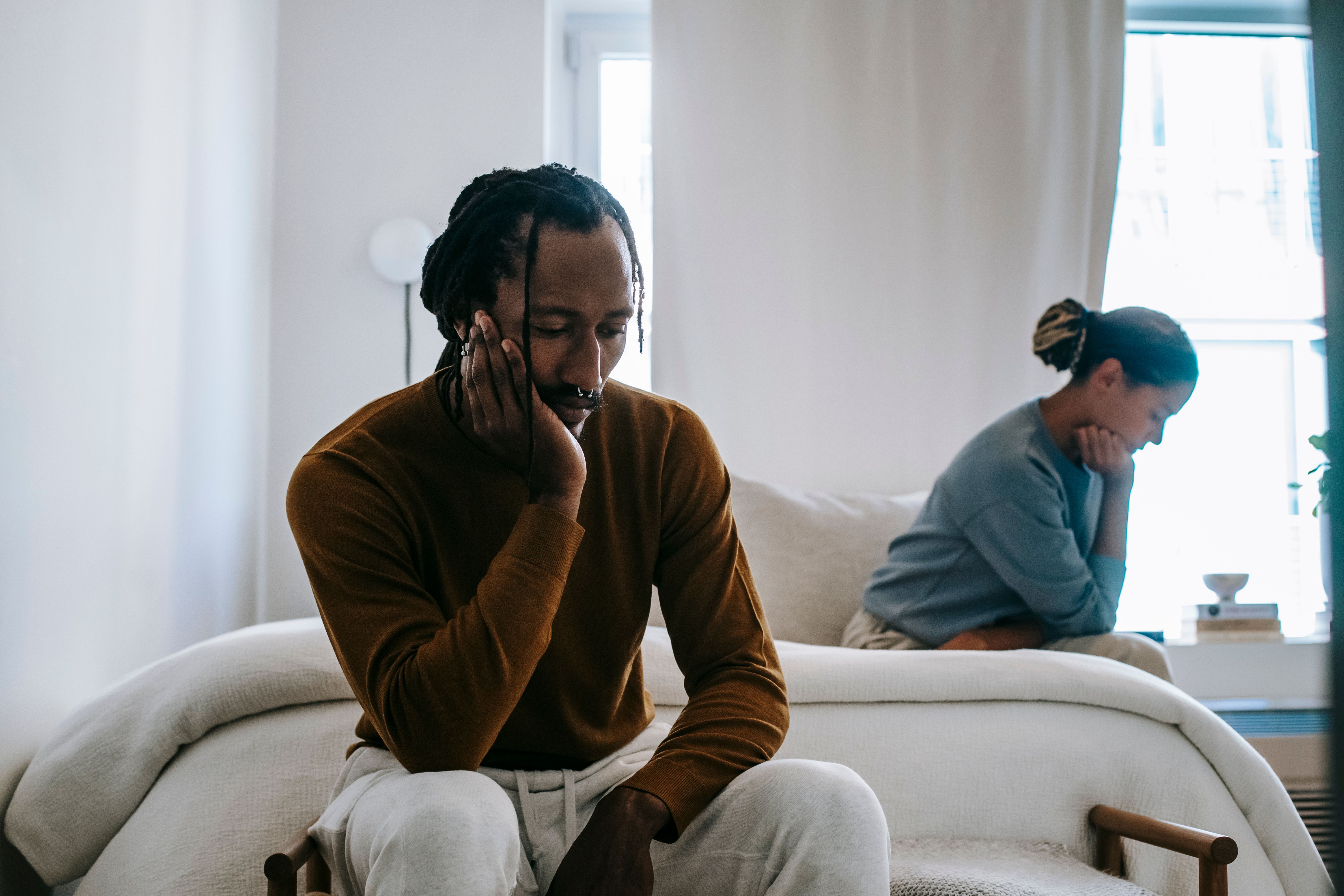 Unhappy African American couple in casual wear during quarrel sitting apart on bed in deep thoughts at home about infidelity 