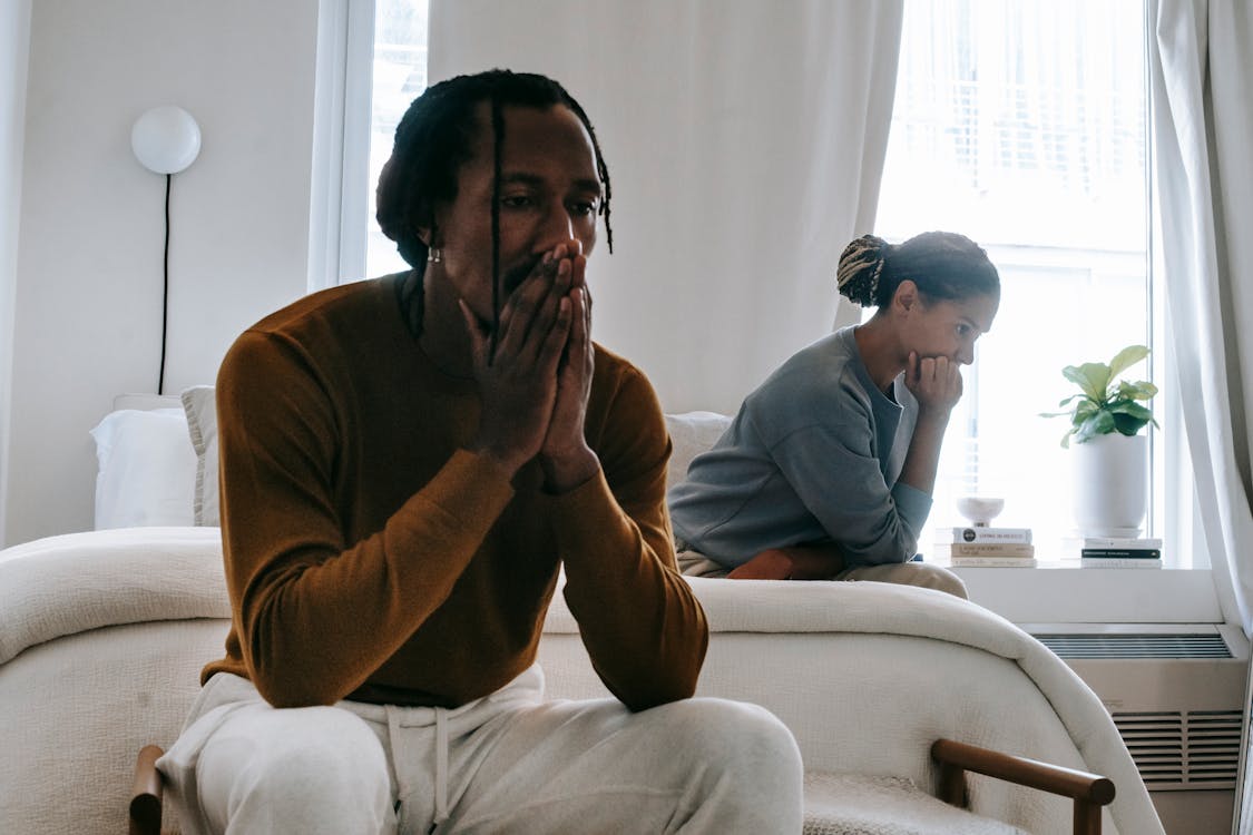 Free Wistful concerned African American couple in casual clothing sitting on bed at home after having quarrel Stock Photo