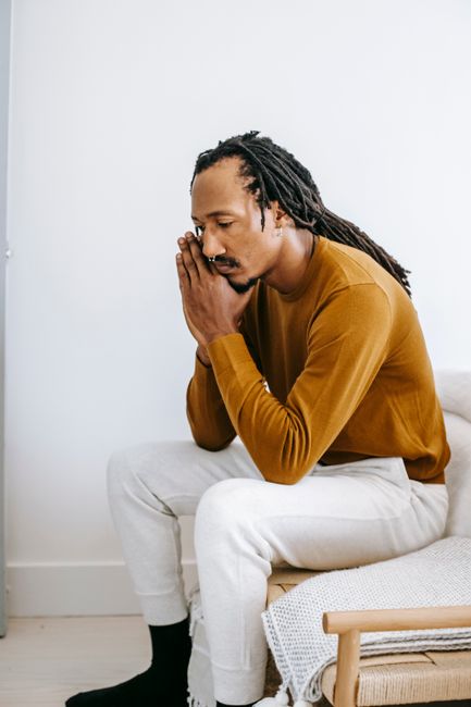 Side view concerned depressed African American male wearing casual outfit touching face in frustration and sitting on couch at home