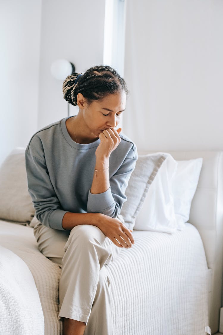 Frustrated Black Woman Touching Lips And Sitting On Bed