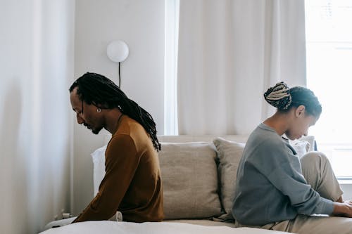Free Side view unhappy sorrowful African American couple sitting on bed back to back after having argument Stock Photo