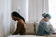 Side view unhappy sorrowful African American couple sitting on bed back to back after having argument