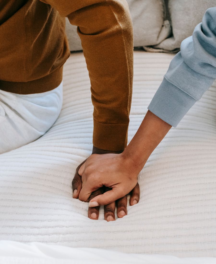 A couple sitting back to back on a bed, holding hands