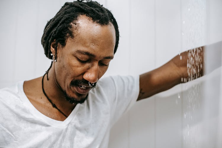 Depressed Black Man Standing In Shower Cabin