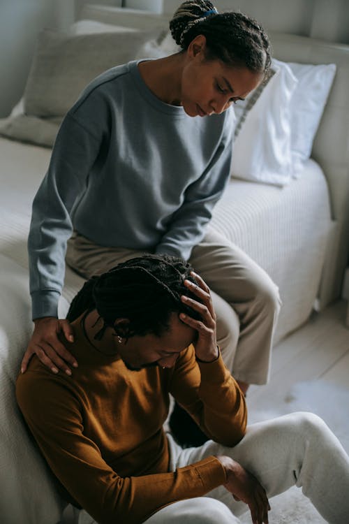 Black wife supporting depressed unhappy husband in bedroom